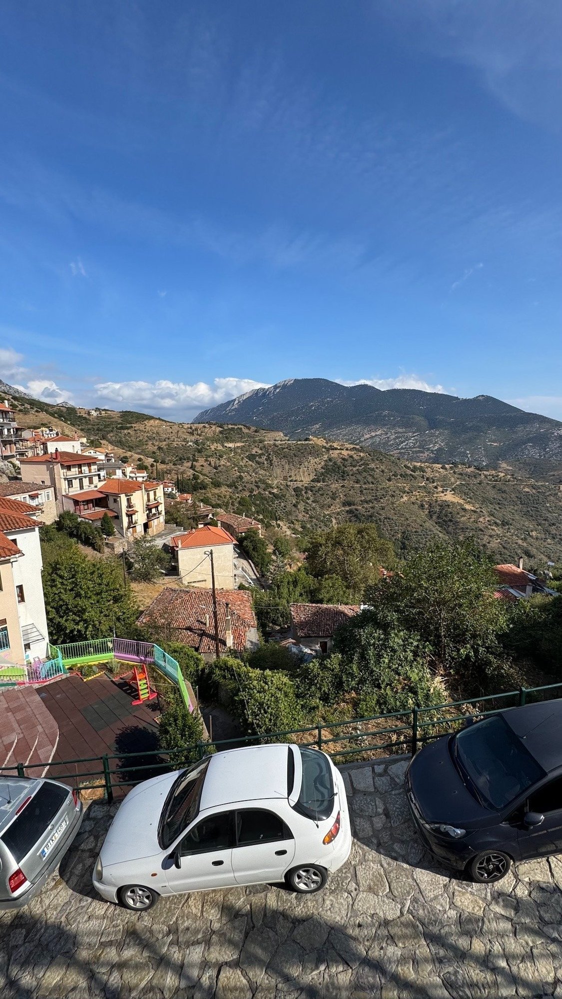 View over a mountain village and green valley near Delphi, with parked cars below