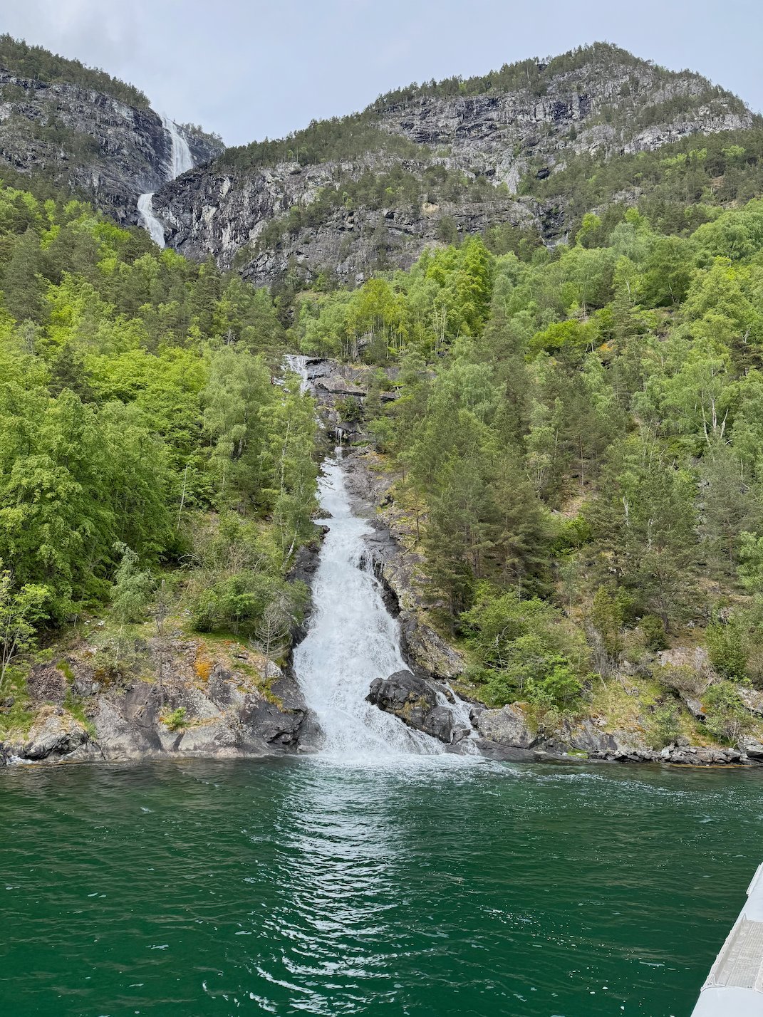 Waterfall that falls into the green water of the fjord, seen from the boat
