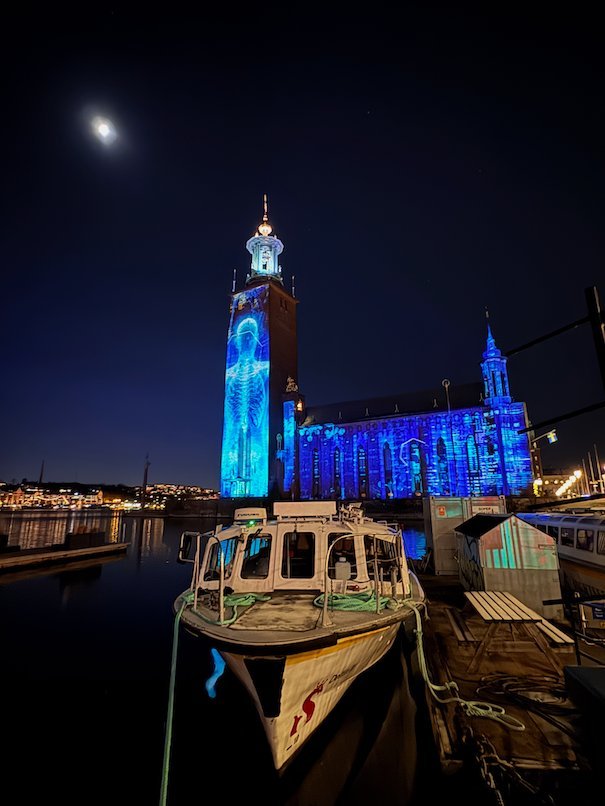 Blue projection of a human body on the tower of Stockholm City Hall, with the full building lit in blue
