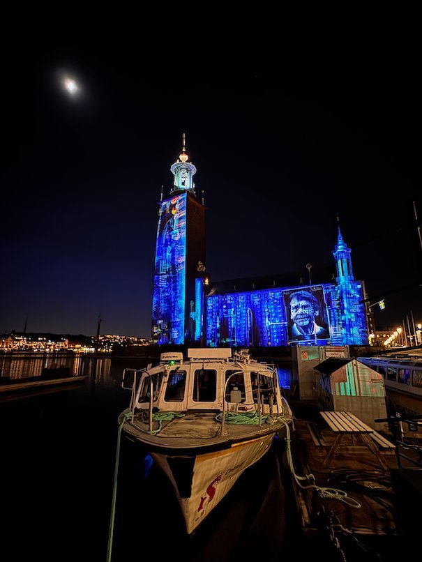 Stockholm City Hall lit in blue, with a portrait of a man projected on the facade