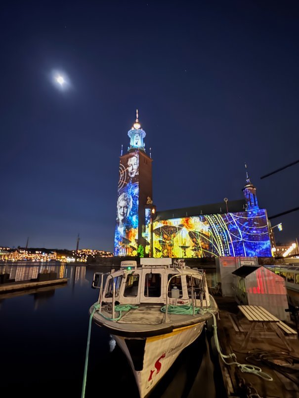Colourful projection with a portrait on the tower of Stockholm City Hall, seen past a moored boat