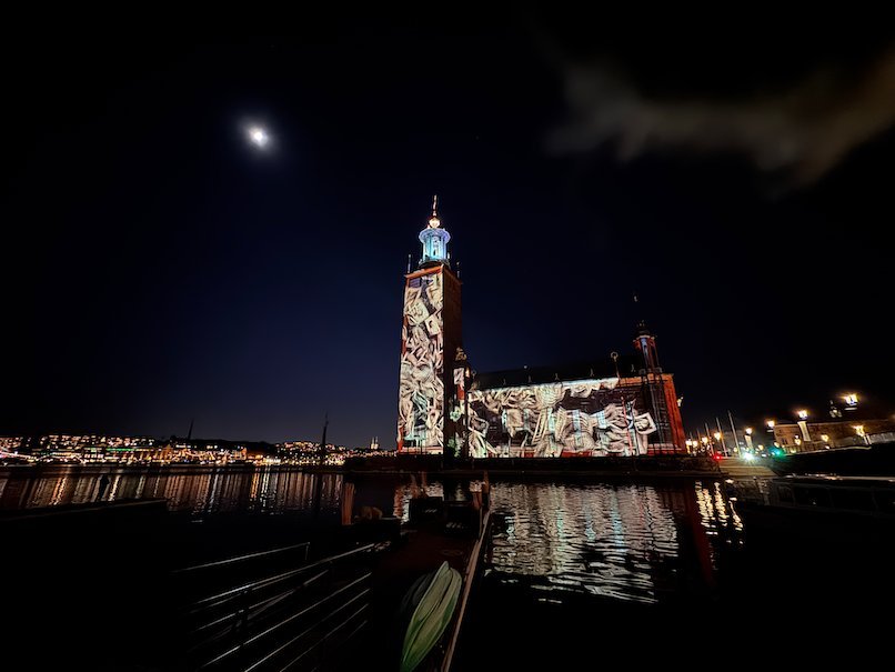 Wide view of Stockholm City Hall with white projections, seen from a jetty across the water