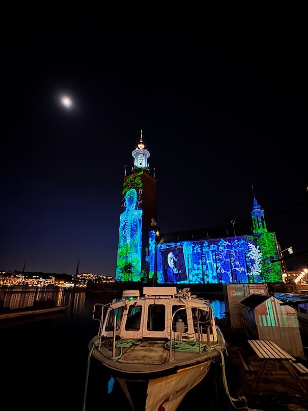 Green human figure projected on the tower of Stockholm City Hall, with blue patterns on the facade