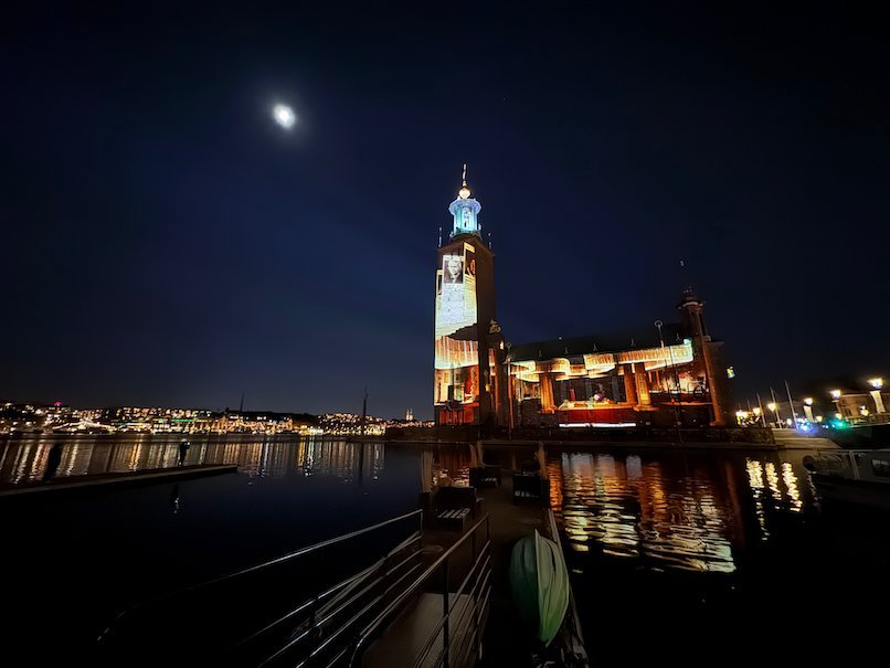 Wide view of Stockholm City Hall with an orange and white projection, seen across the water at night