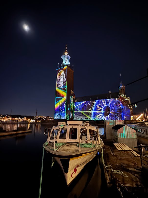 Rainbow stripes on the tower and a large wheel pattern on the facade of Stockholm City Hall at night