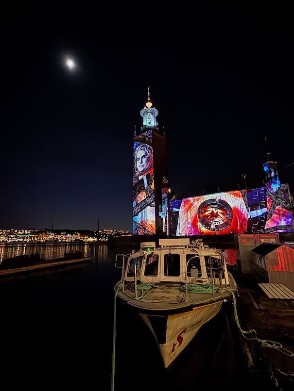 Red and pink projection of an eye on the facade of Stockholm City Hall, with a portrait on the tower