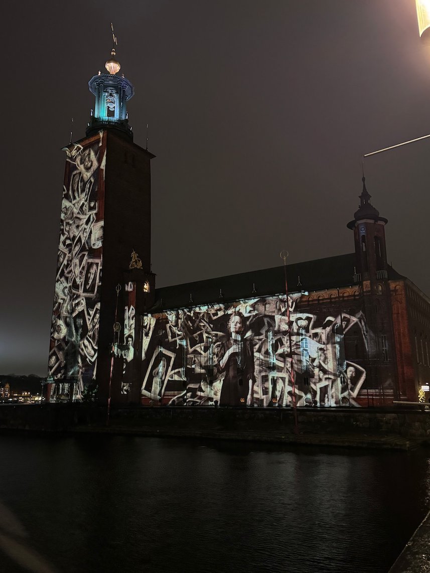 White line drawings of people projected on the tower and facade of Stockholm City Hall on a cloudy night