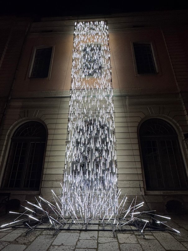 Cascade of white light tubes falling down a building facade and spreading over the pavement