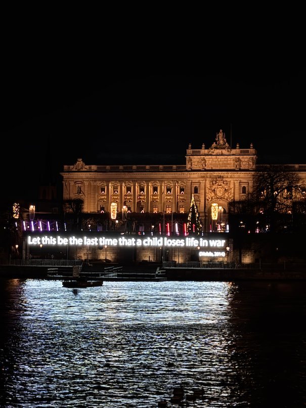 The Swedish Parliament building lit up at night, with the text Let this be the last time that a child loses life in war shown by the water