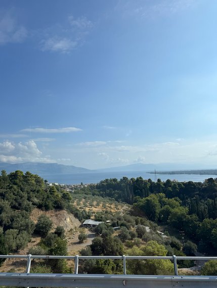 Olive groves, green hills and the sea seen from the road to Meteora