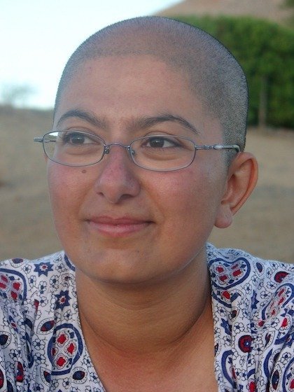 Zayera Khan with a shaved head and glasses smiles outdoors at a camp by the Orange River.