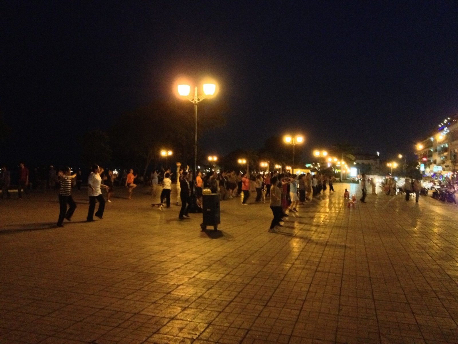 Groups of people do aerobics on a lit promenade in Phnom Penh at night.