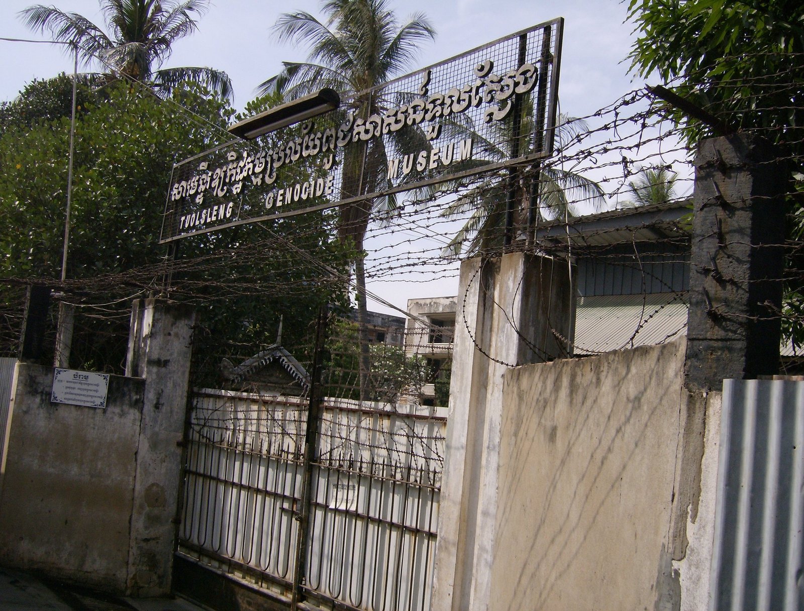The entrance gate of Tuol Sleng Genocide Museum in Phnom Penh has barbed wire and a sign in Khmer and English.