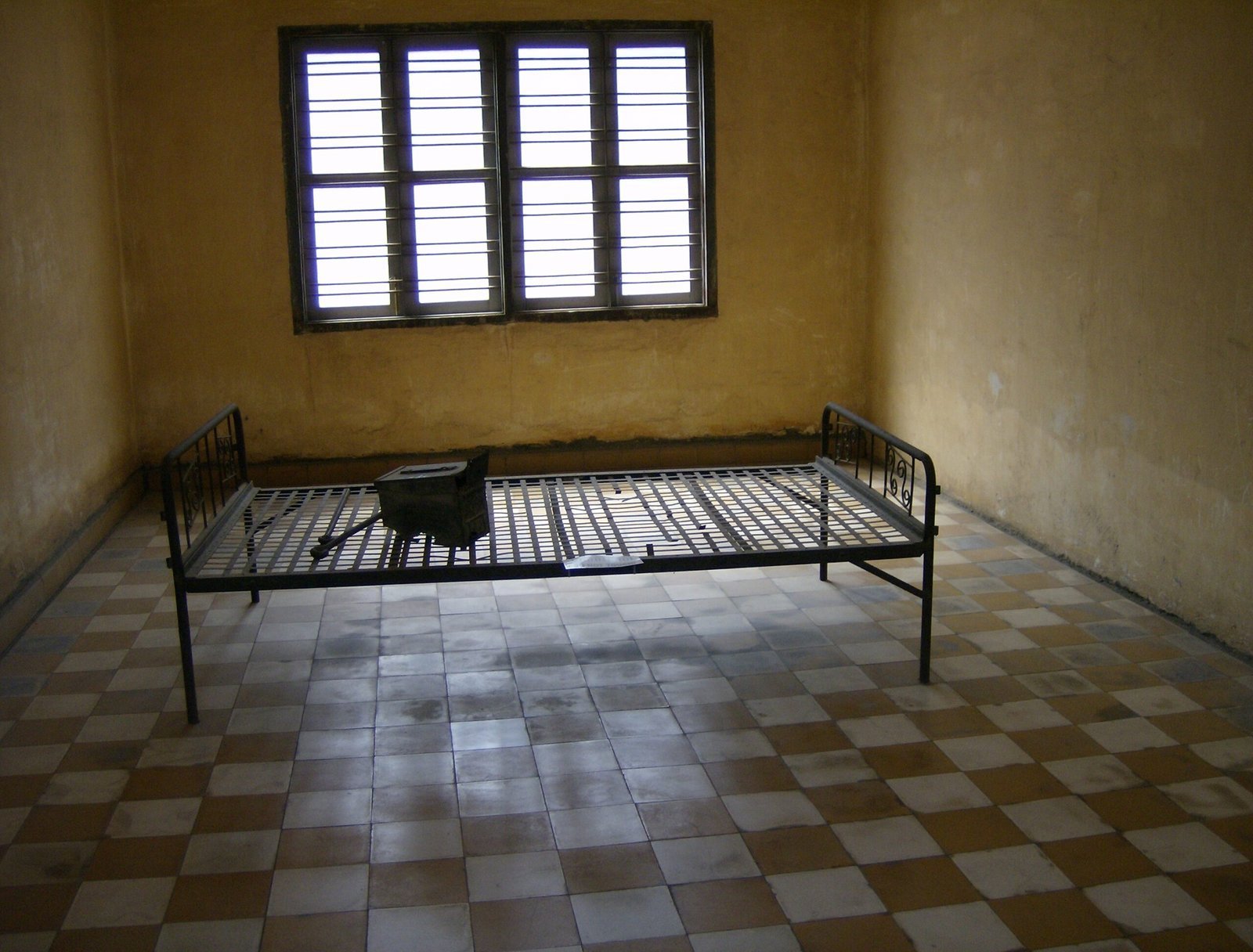 A metal bed frame stands in an empty room with a tiled floor at Tuol Sleng in Phnom Penh.