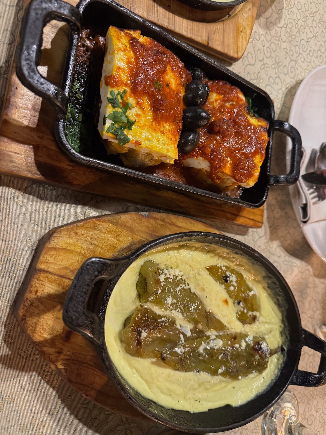 Two baked dishes with cheese and peppers sit in black pans on a restaurant table in Pristina.