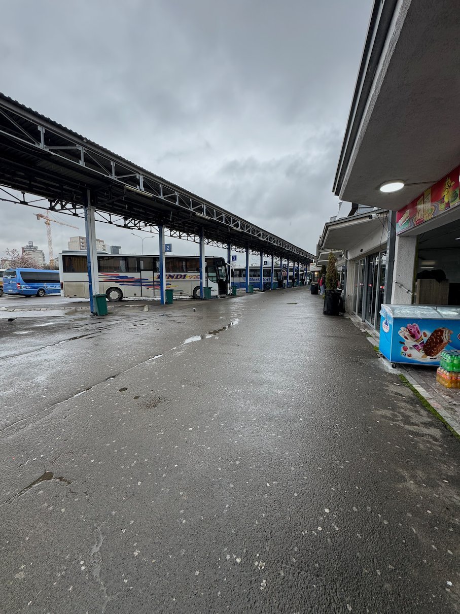 Buses wait under a long roof at the bus station in Pristina on a rainy day.