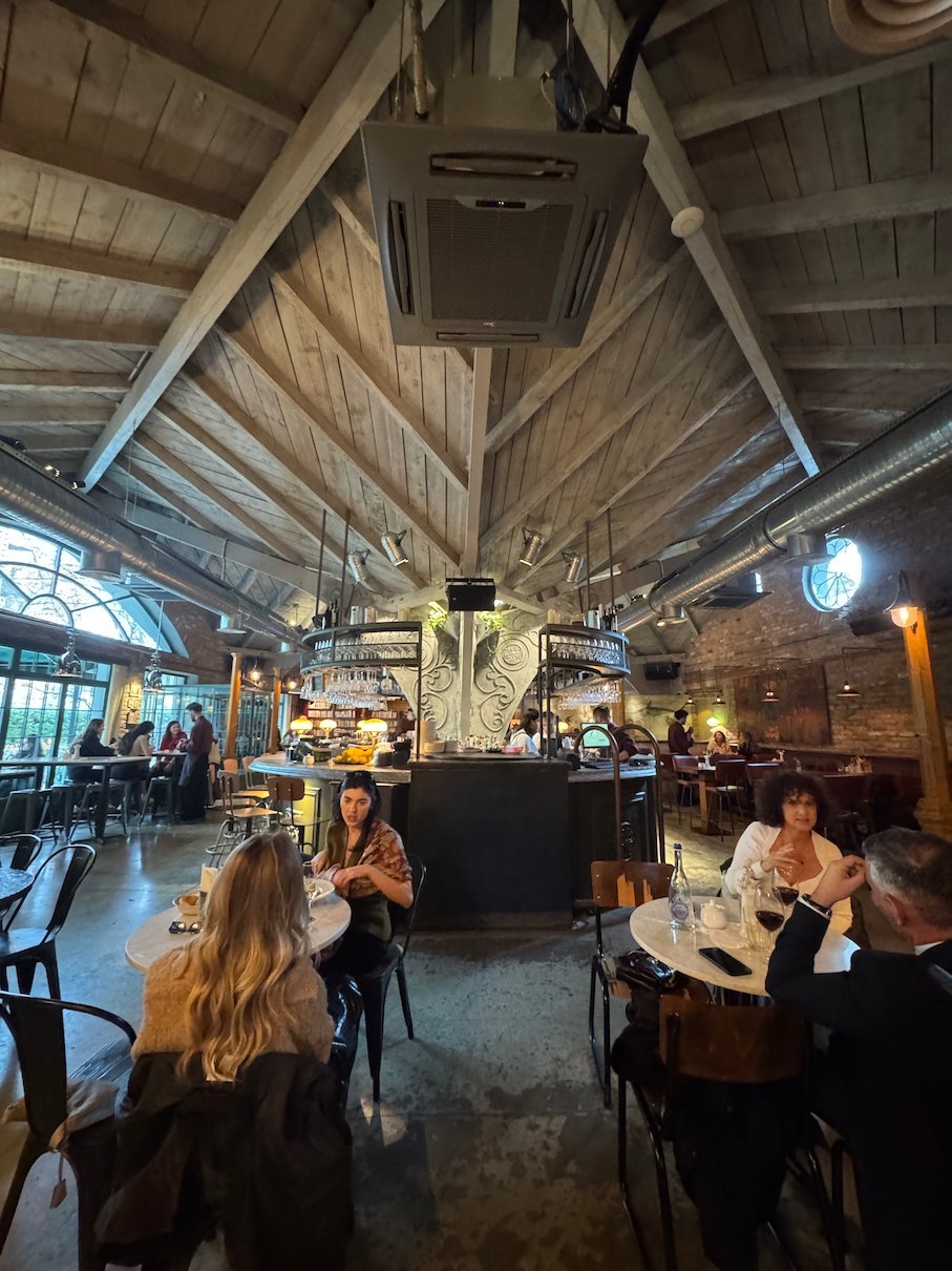 People sit at tables under a high wooden roof in a busy cafe in Pristina.