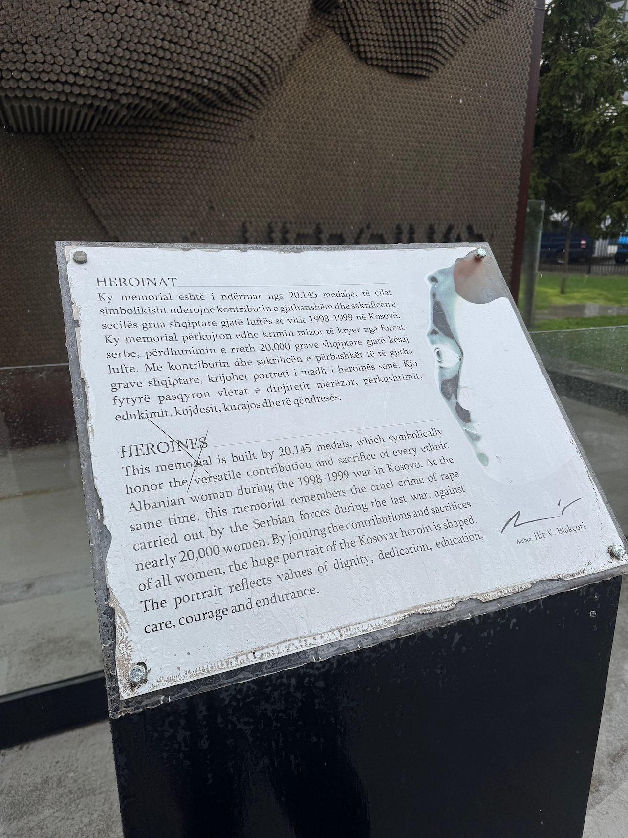 A text plaque in Albanian and English explains the Heroinat memorial in Pristina.