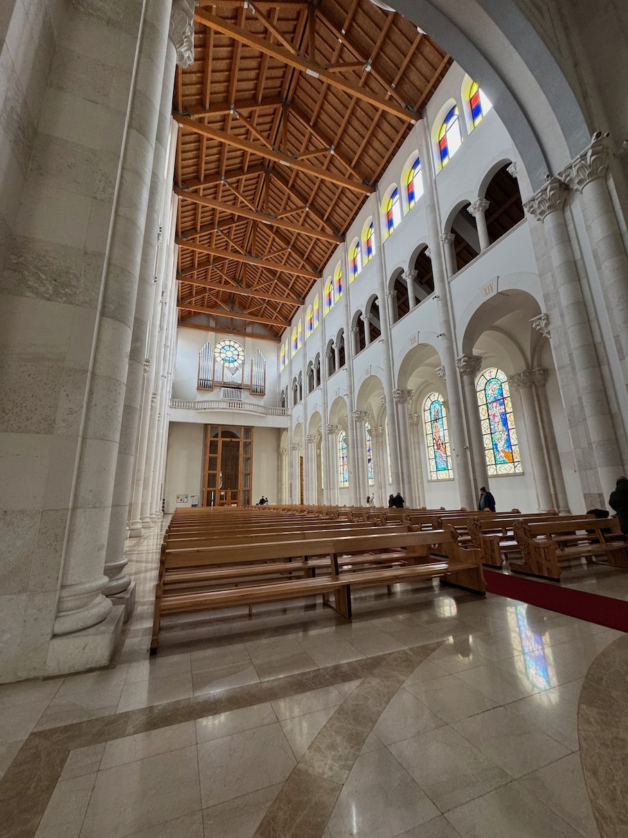 Wooden pews and stained glass windows fill the bright nave of the Cathedral of Saint Mother Teresa in Pristina.