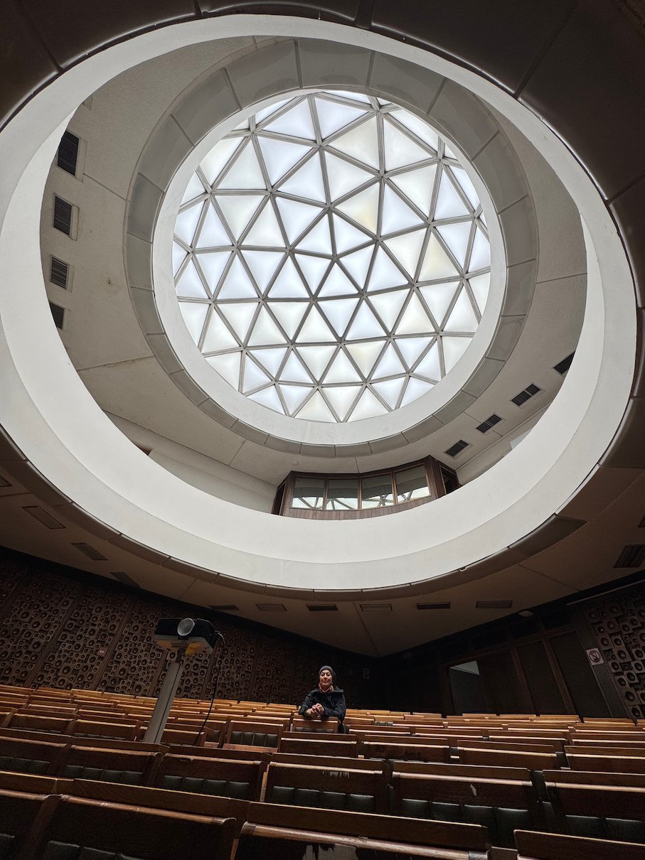 A traveler sits alone in the auditorium below the geodesic dome of the National Library in Pristina.