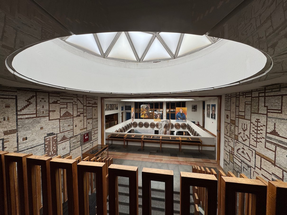 A round skylight lights a hall with patterned walls and wooden seats in the National Library in Pristina.