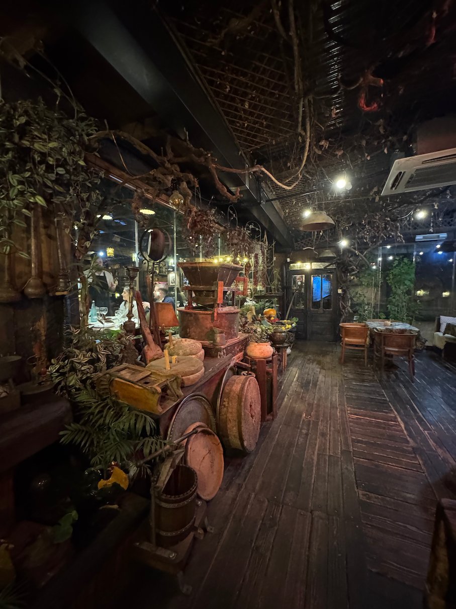Copper pots, plants and warm lights fill a dark wooden restaurant interior in Pristina.