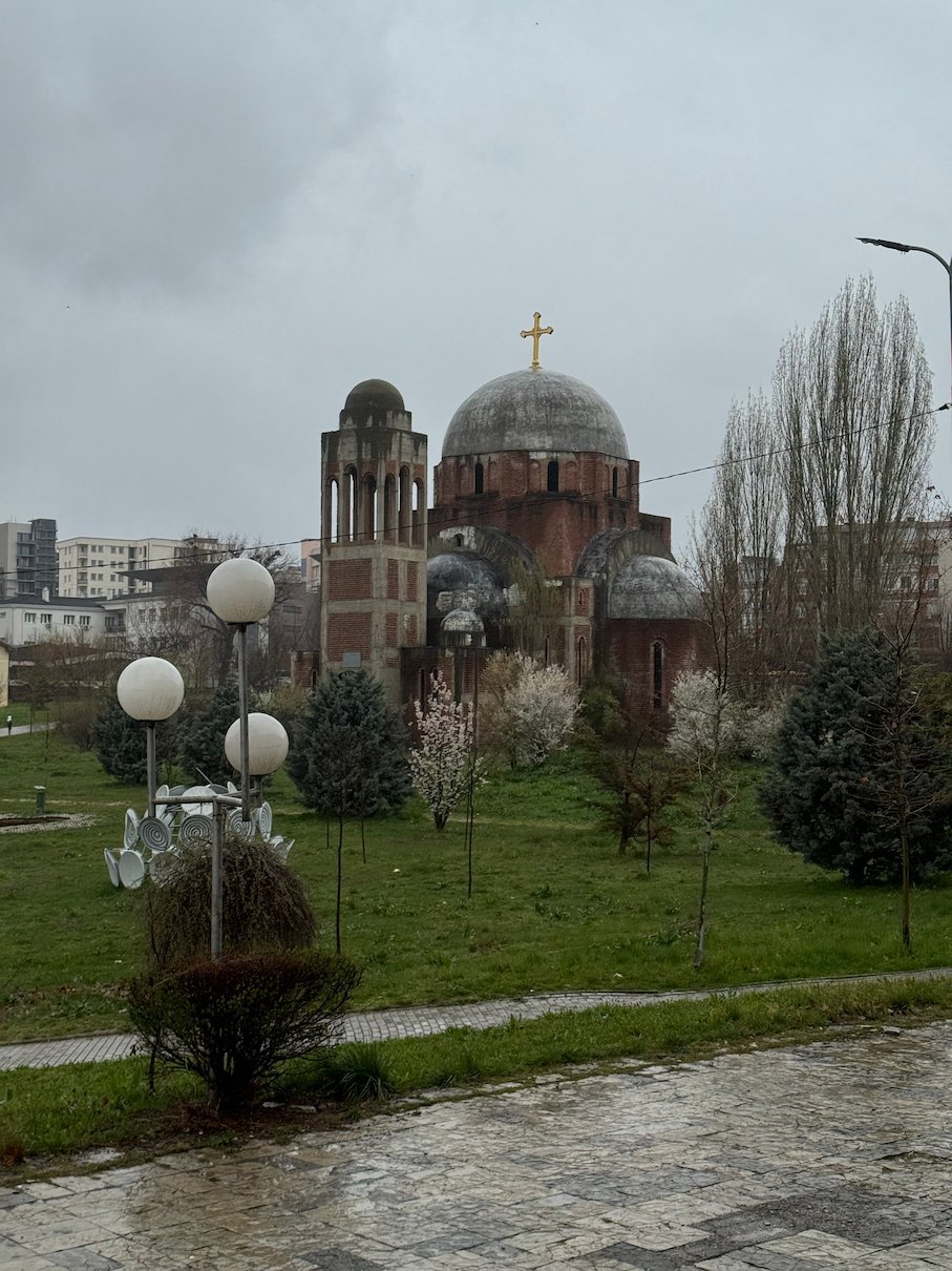 An unfinished Orthodox church with brick domes stands in a park on the university grounds in Pristina.