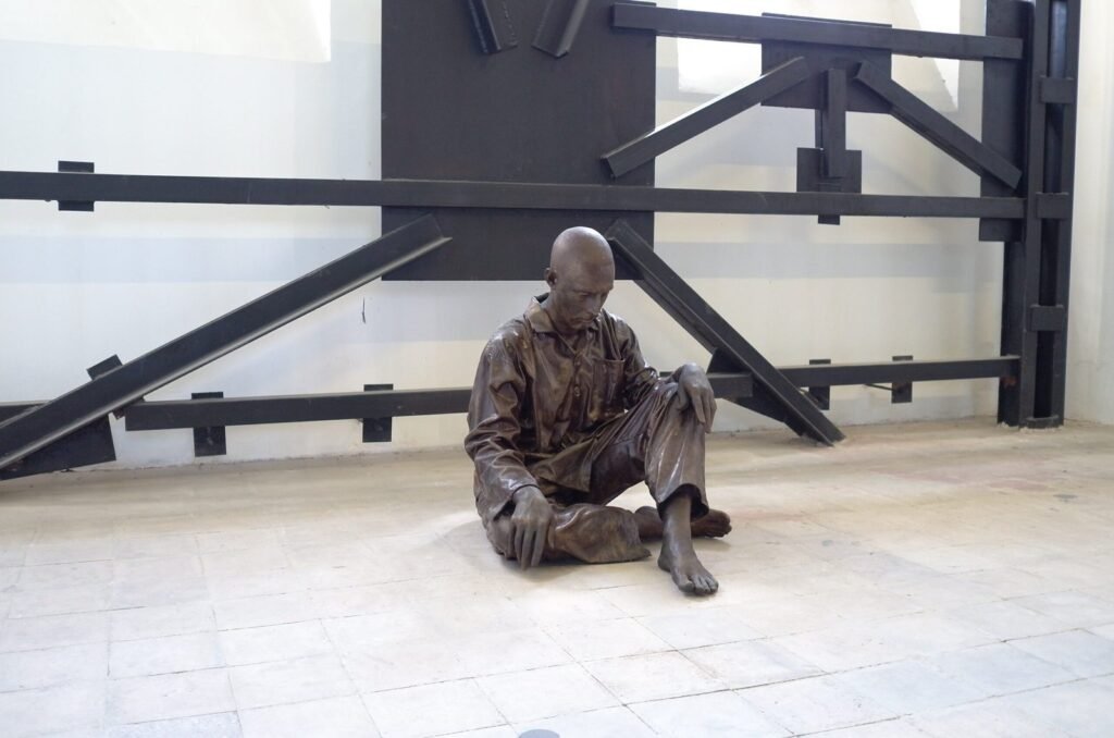 Bronze figure of a prisoner who sits on the floor of a cell