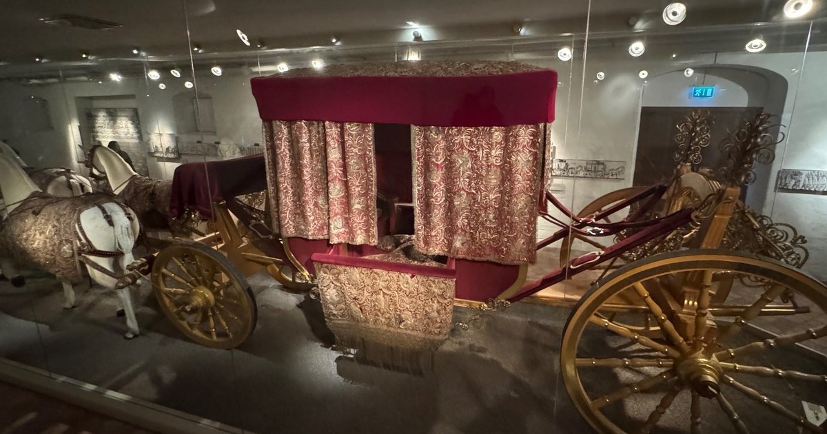 Queen Kristina’s coronation coach from 1650 behind glass, with gilded wheels, red and gold embroidered curtains and white model horses.