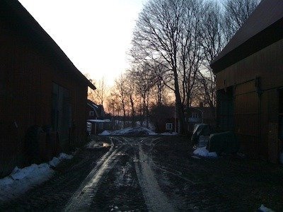 Lerig gårdsväg mellan röda lador i solnedgång