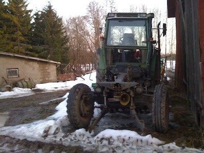 Gammal grön traktor på en lerig gårdsplan med snö