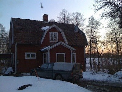 Rött boningshus med vita knutar och en bil på gården, snö på marken