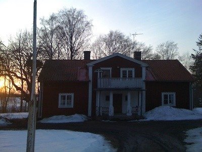 Rött tvåvåningshus med vit veranda och balkong, snö på marken