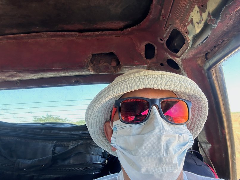 Zayera Khan in a hat, sunglasses and mask takes a selfie in a bush taxi.