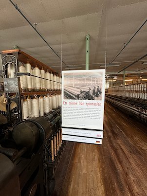 Spinning machines with white bobbins and a banner Ett minne från spinnsalen