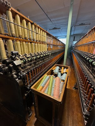 Spinning frame with rows of bobbins and a box of coloured yarn