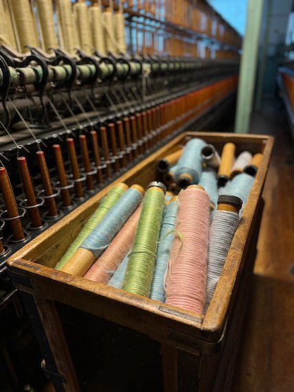 Wooden box of pastel yarn bobbins beside a spinning frame
