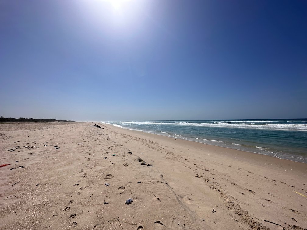 The sun shines over a long beach with many tracks in the sand.