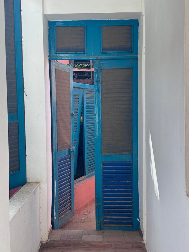 Tall blue doors with shutters stand at the end of a white corridor.