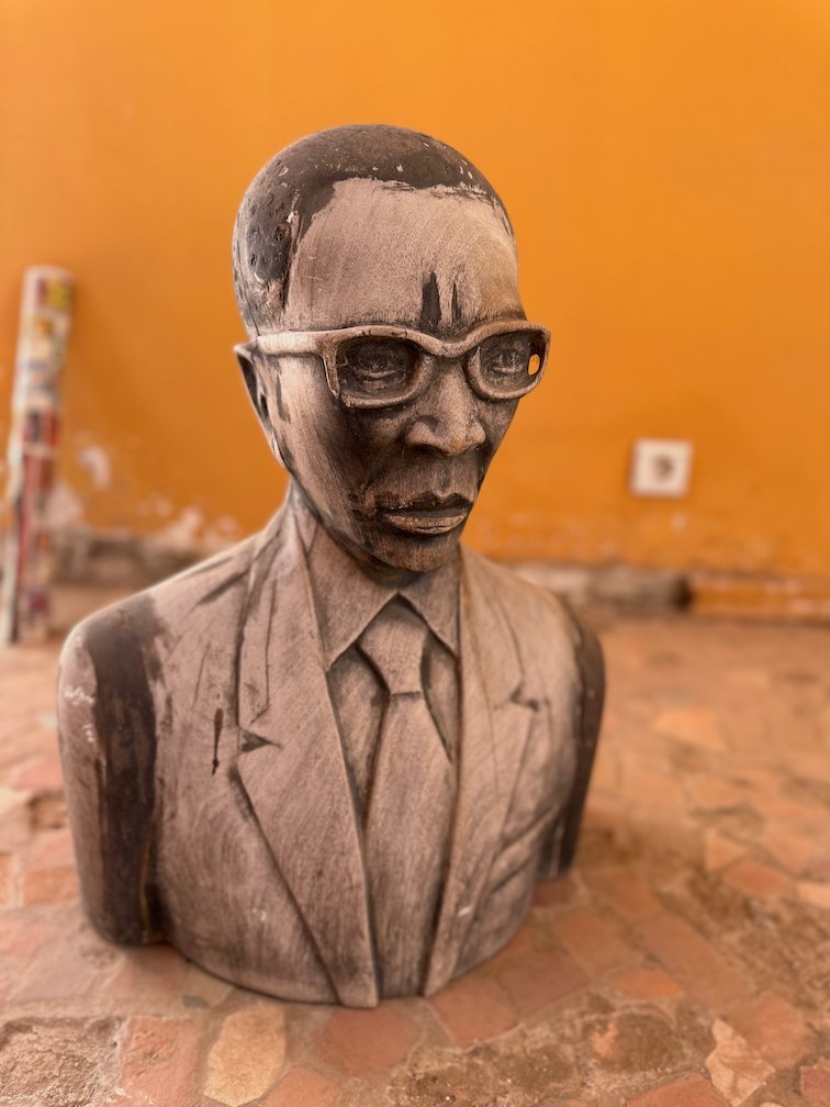 A stone bust of a man with glasses stands in an orange room.