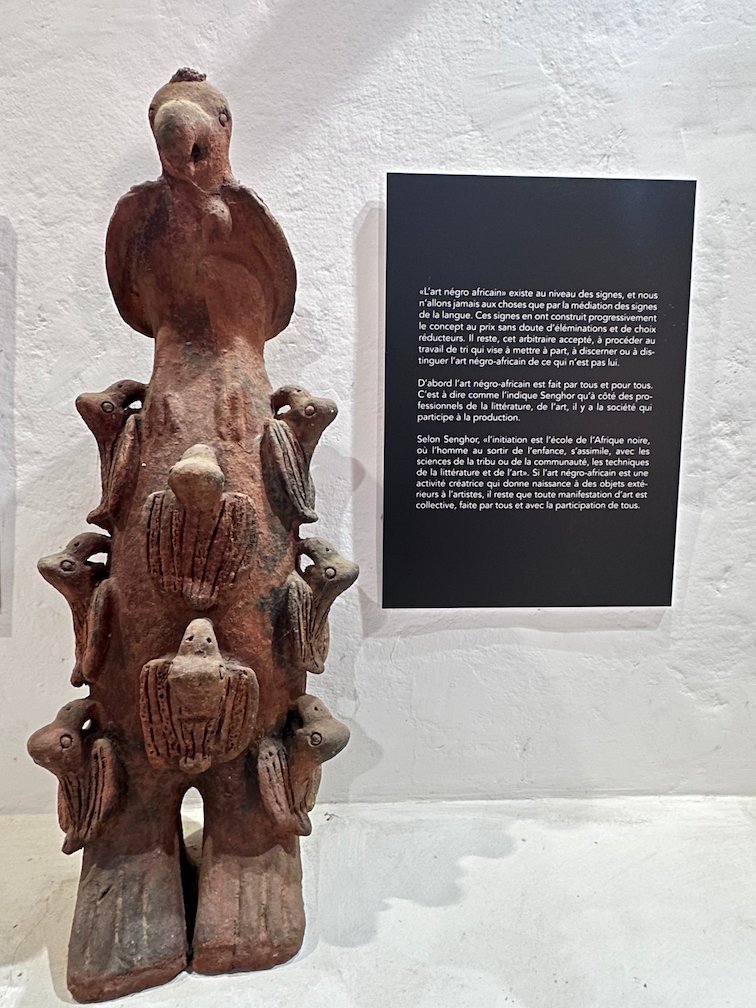 A clay sculpture with a bird on top stands next to a text panel.