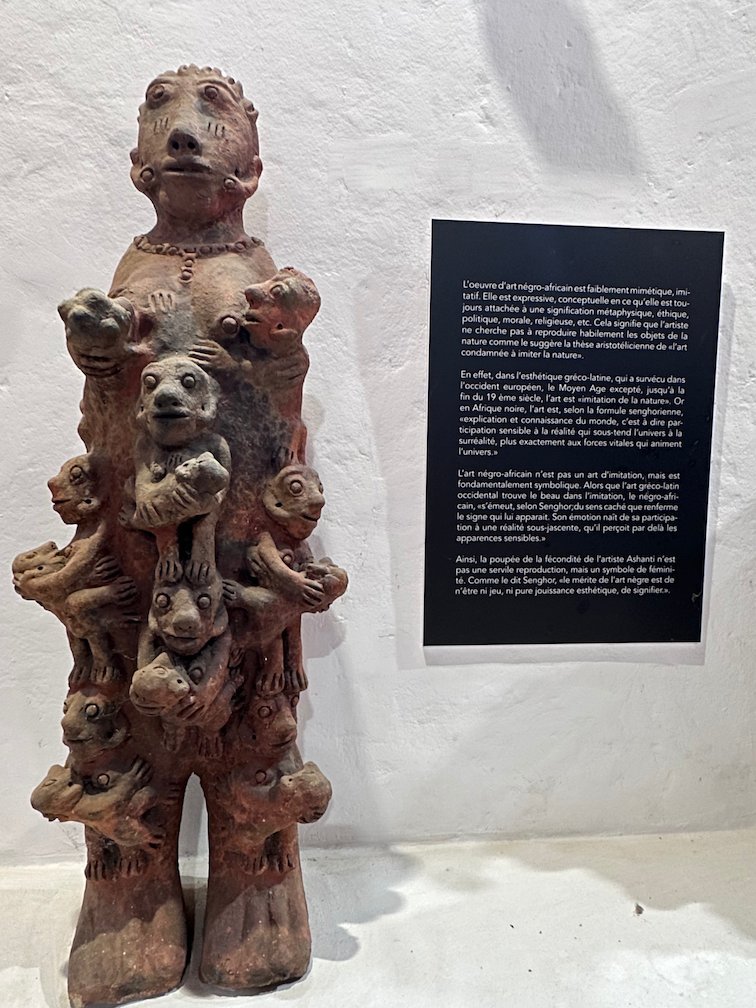 A tall clay sculpture with animal figures stands in a gallery in Saint-Louis.