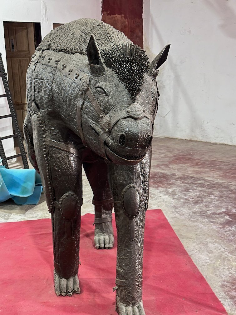 A big metal animal sculpture stands on a red carpet in a gallery.