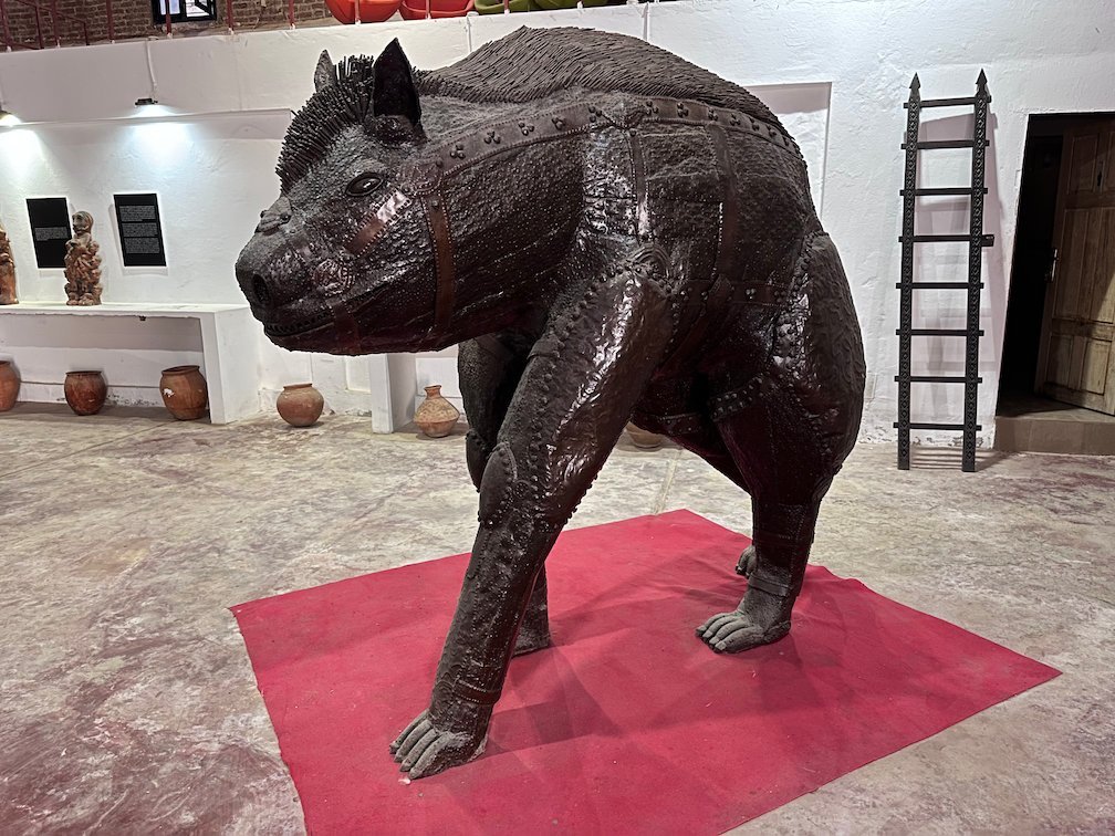 A large metal sculpture of a hyena stands on a red carpet in a gallery.
