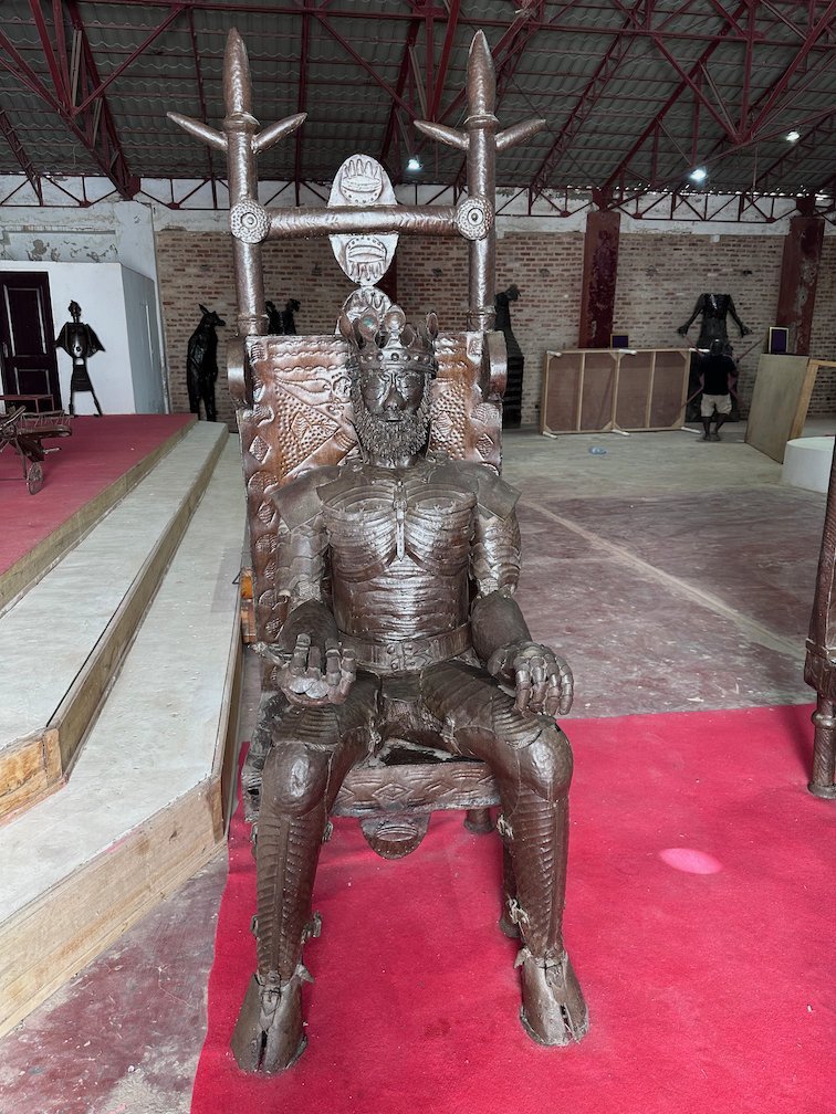 A metal sculpture of a king on a throne stands in a gallery.