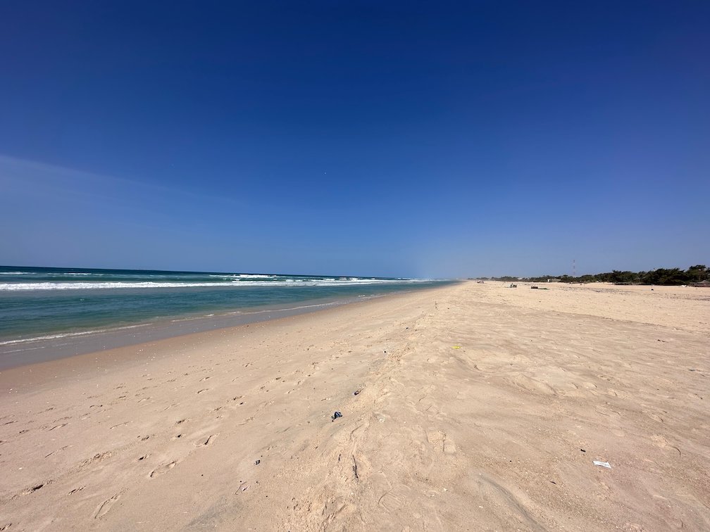 A long empty beach runs along the ocean under a deep blue sky.