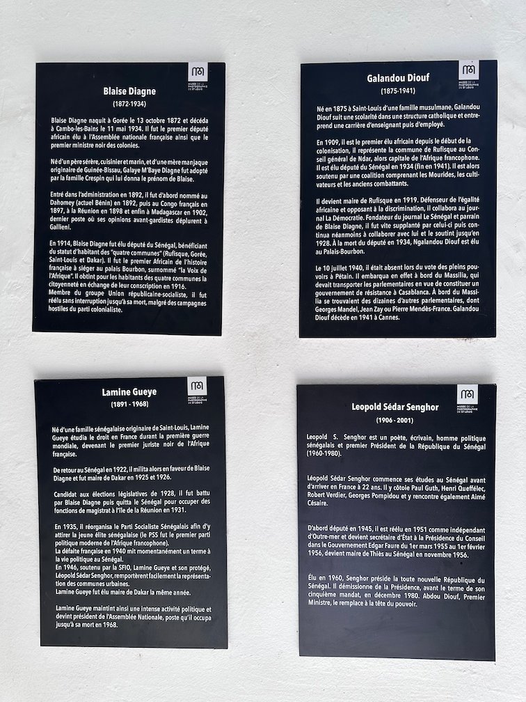 Black panels with short life stories hang on a wall in Saint-Louis.