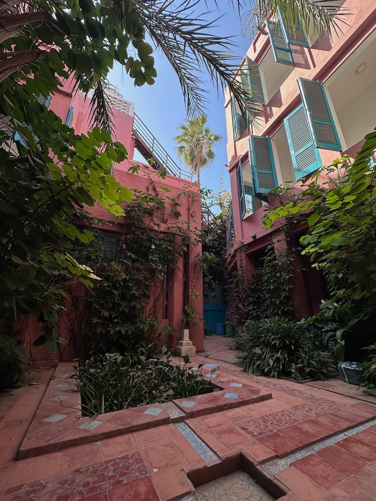 A courtyard with pink walls, blue shutters and plants in Saint-Louis.