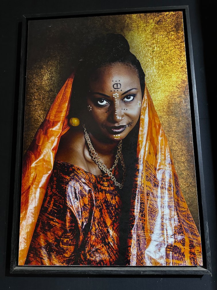 A framed portrait shows a woman with face paint and an orange scarf.