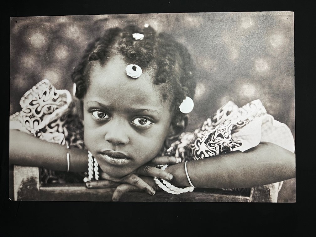 A black and white portrait shows a young girl with her head on her hands.